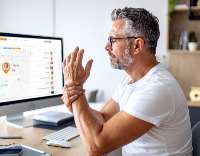 Man holding wrist while using desktop computer